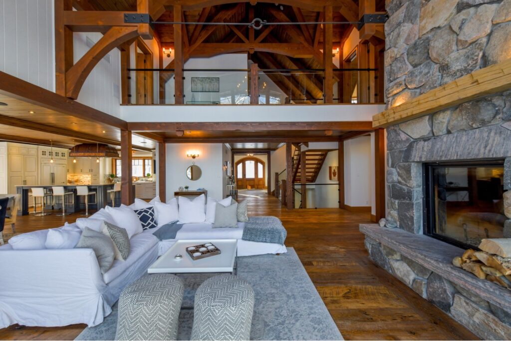 Spacious open-concept living area featuring exposed timber beams, natural stone fireplace, and handcrafted wood flooring by Bedrock Finishes.